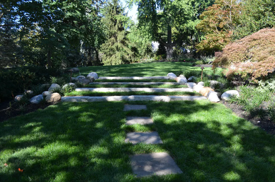 Wide stone slab steps with boulders set into a lawn slope under shade trees